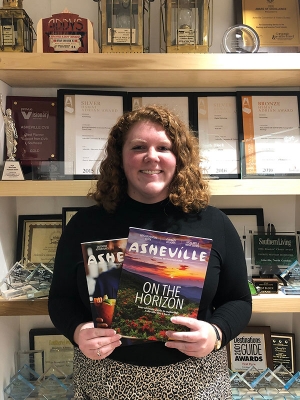 Appalachian alumnus Glenn Ramey ’19 at the Explore Asheville Convention and Visitors Bureau, where she works as a group sales and service specialist. Ramey, who is pictured holding two visitor guides published by the bureau, graduated summa cum laude from Appalachian in 2019 with a B.A. in theatre arts and minors in general business and nonprofit management. Photo submitted